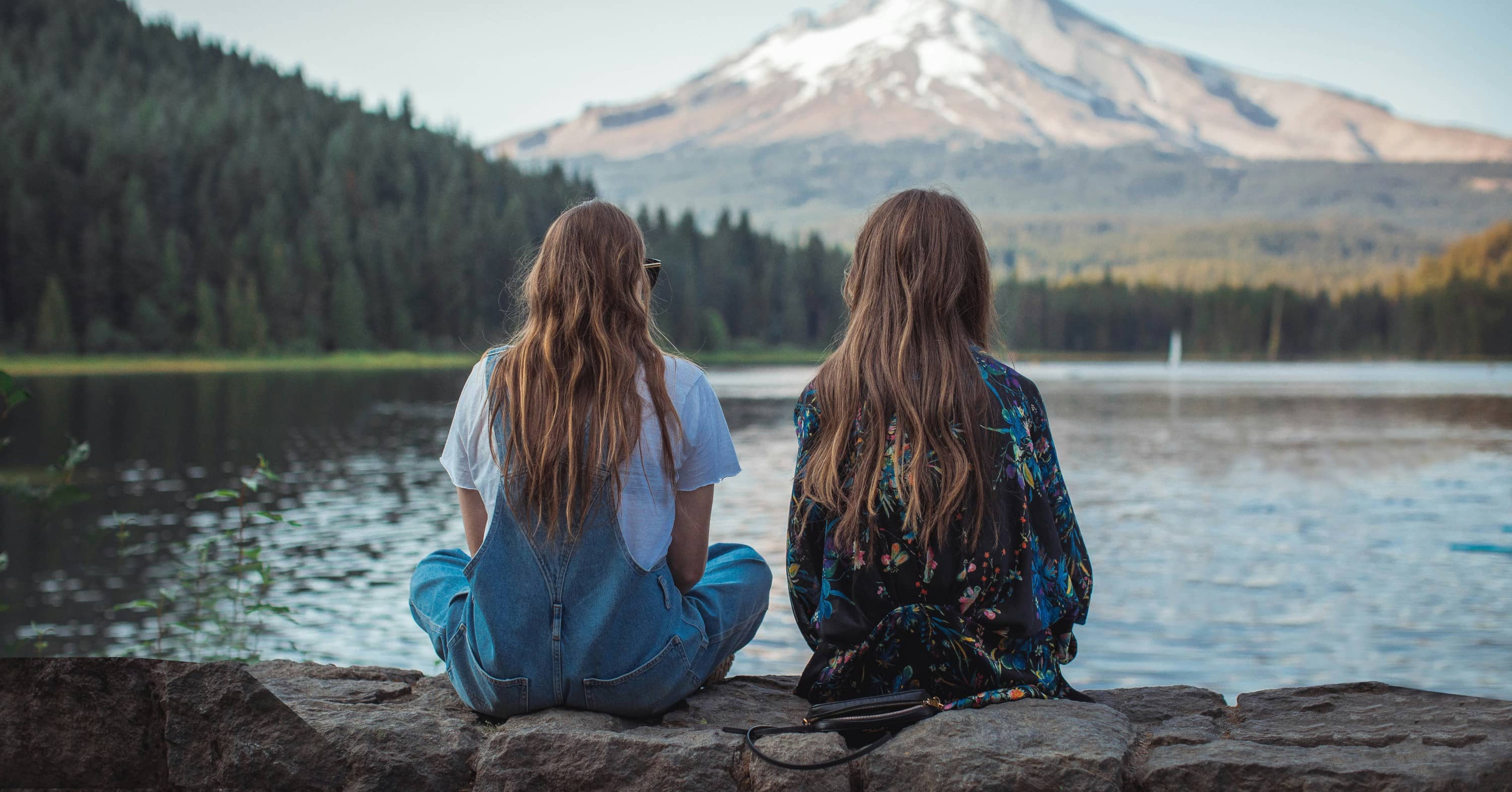 women sitting on rock near body of water